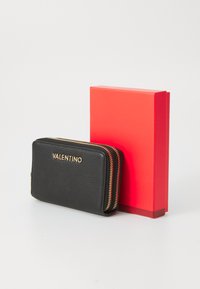 Schwarze strukturierte Lederbrieftasche mit goldenen Beschlägen und Reißverschluss, neben einer hellroten rechteckigen Geschenkbox präsentiert.