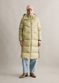 Μακρύ πούφο παλτό σε ανοιχτό πράσινο χρώμα με φερμουάρ μπροστά, κουκούλα και ραφές. Φορεμένο με φαρδιά μπλε τζιν και καφέ μποτάκια μέχρι τον αστράγαλο.