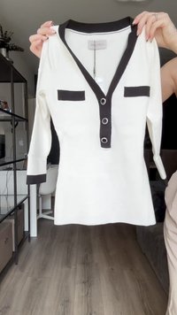 Weißes Langarmshirt mit schwarzem V-Ausschnitt, drei Knöpfen mit silbernen Akzenten und zwei schwarzen Taschen auf der Brust.