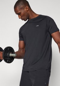 Sort atletisk t-shirt med korte ærmer, tætsiddende design, glat tekstur og et lille logo på brystet, parret med mørke shorts.