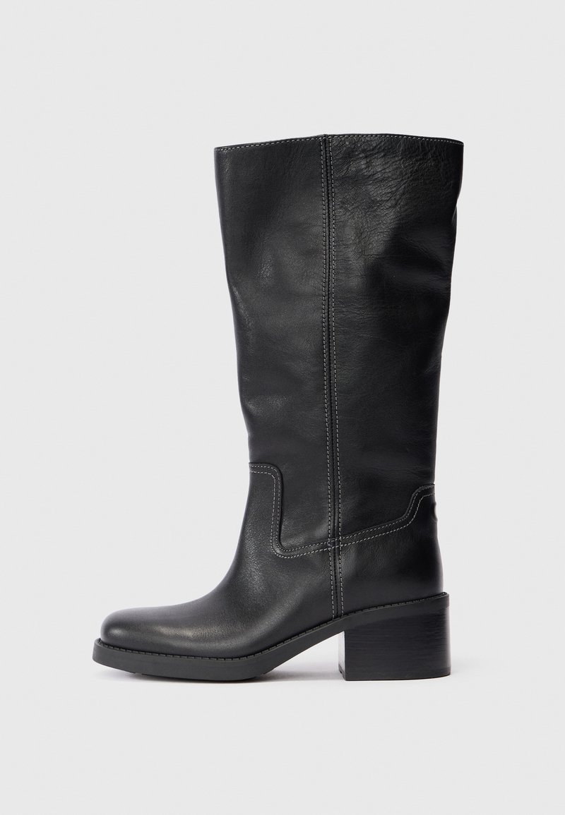 Bota alta de cuero negro con punta redondeada, costura vertical y tacón cuadrado. Textura suave con un acabado mate.