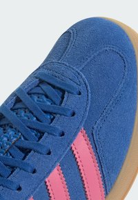 Modré semišové tenisky s ružovými pruhmi, s textúrovaným povrchom, okrúhlymi šnúrkami a béžovou gumovou podrážkou.