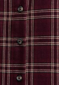 Camisa de cuadros burdeos con textura de franela, con líneas negras, beige y rojas que se intersectan, y botones negros.