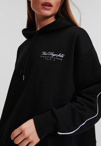 Zwarte hoodie van katoen, met een trekkoord, ribgebreide manchetten en witte logotekst met accenten. Gladde textuur en een relaxte pasvorm.