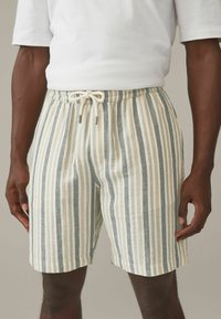 Shorts rayés en beige, bleu et crème. Fabriqués en tissu léger avec une taille élastique et un cordon de serrage ajustable.