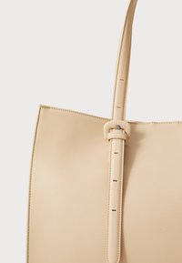 Beige leren tote bag met een gestructureerd ontwerp, verstelbare schouderriem en subtiele stiksels. Heeft een gladde textuur en strakke lijnen.