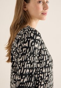 Top a maniche lunghe con base nera e un motivo astratto monocromatico a contrasto. Realizzato in materiale morbido, offre una vestibilità rilassata.