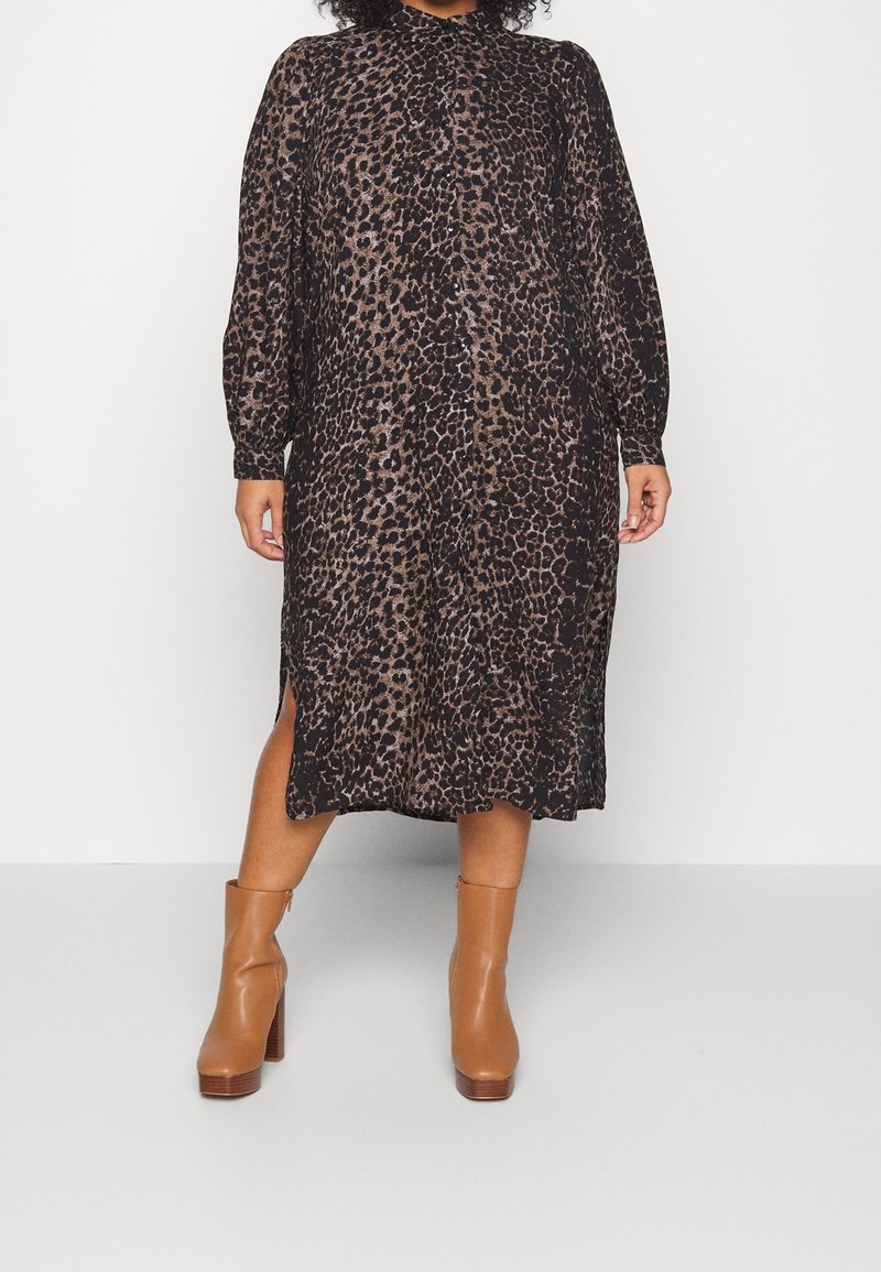 Robe midi à imprimé léopard en tissu transparent, avec des manches longues, un col montant, des fentes latérales, et associée à des bottines à talons brunes.