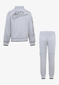 Training suit Nike gri featuring a jachetă cu fermoar cu logo pe spate și pe manșon, plus pantaloni jogger asortați cu mansete canal și detalii la buzunare.