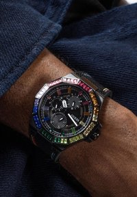 Reloj octogonal negro con coloridos gemstones cuadrados, diales de cronógrafo y una correa texturizada. La caja presenta detalles multicolores alrededor del bisel.