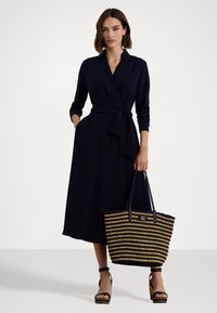 Jūras spēku krāsas apģērbs ar garajām piedurknēm un sasietu vidukli, apvienots ar svītrotu austu somu, kas izgatavota no melnā un dabīgā šķiedras, ar zelta logotipu.