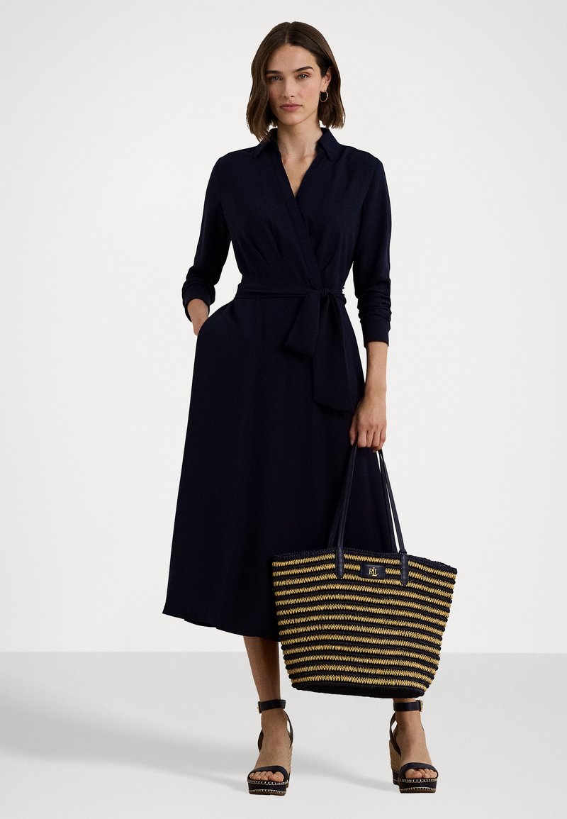 Jūras spēku krāsas apģērbs ar garajām piedurknēm un sasietu vidukli, apvienots ar svītrotu austu somu, kas izgatavota no melnā un dabīgā šķiedras, ar zelta logotipu.