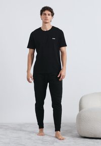 Μαύρο βαμβακερό T-shirt με μικρό λογότυπο, συνδυασμένο με μαύρο τζόκερ σετ. Μαλακή υφή και άνετη εφαρμογή, σε ουδέτερο φόντο.