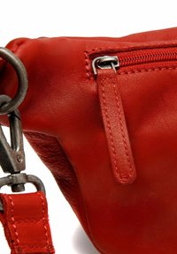 Röd läderhandväska med dragkedjestängning, en mjuk yta, avtagbar rem och silverfärgade dragkedjor och hårdvarudetaljer.