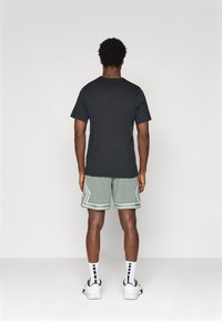 Svart kortermet t-skjorte, grønne nettingshorts med hvite detaljer, hvite sokker med svarte striper, og joggesko. Synlig bakfra.