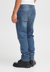 Mėlynos džinsinės kelnės su tiesiais kojų apačios siūleliais, pašviesėjusios šlaunų srityje, su dviem užpakalinėmis kišenėmis. Derinamos su juodais aulinukais su raišteliais.