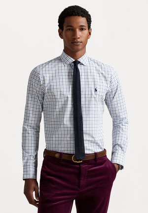 Wit overhemd met een blauw en bruin ruitpatroon, lange mouwen en een kraag, gecombineerd met een bruine leren riem en donkerpaarse corduroy broek.