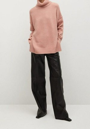 Personne porte un pull rose oversize à col roulé avec des manches longues et un pantalon en cuir noir à jambes larges sur un fond clair.