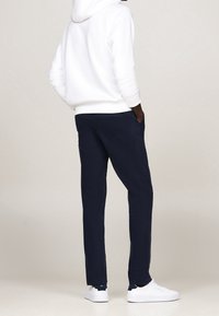 Pantaloni della tuta blu navy in una vestibilità comoda, con vita regolabile tramite cordoncino e tasche laterali, abbinati a una felpa bianca e sneakers bianche.
