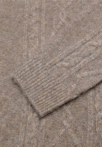 Beżowy sweter w splot kablowy, wykonany z miękkiej wełny, z fakturowanym wzorem i ściągaczami, podkreślający przytulny i ciepły design.