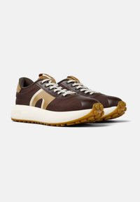 Brown athletic shoes with a textured fabric upper, cream midsole, and rubber outsole featuring a patterned grip, detailed with tan accents.