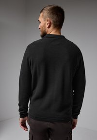 Svart stickad tröja med en texturerad yta, långa ärmar och en avslappnad passform. Har en liten krage och ribbade mudd och nederkant.