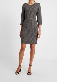 Sort-hvid stribet, tætsiddende kjole med trekvartærmer, rund halsudskæring og taljeaccent. Et par sorte højhælede sandaler.