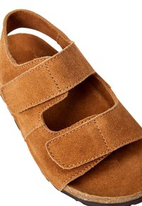 Sandale en suède marron avec deux sangles réglables à boucle auto-agrippante. Conception ouverte avec des zones découpées et une semelle intérieure texturée. Semelle durable.