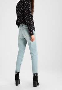 Haut noir à manches longues à motifs floraux avec encolure ronde, jean bleu clair taille haute, et bottes à talons épais noires. Design de tenue décontractée.