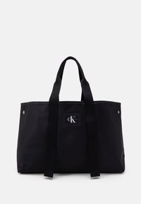 Black tote bag with a rectangular shape, made of durable material, featuring two sturdy handles, a logo patch, and silver hardware accents.