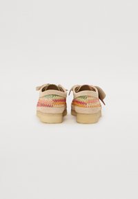 Des chaussures beiges avec une finition texturée, dotées d'un motif tissé coloré en rose, orange et vert. Semelles en caoutchouc de couleur claire.