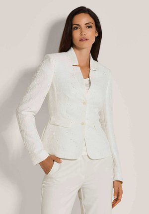 Weißer strukturierter Blazer mit Reverskragen, zwei vorderen Taschen und zwei Knöpfen. Über einem hellen Oberteil getragen und mit weißen Hosen kombiniert.
