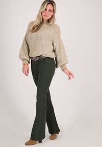 Beige gebreide trui met ballonmouwen, gecombineerd met donkergroene uitlopende spijkerbroeken en een met studs versierde zwarte riem, met een gladde textuur.