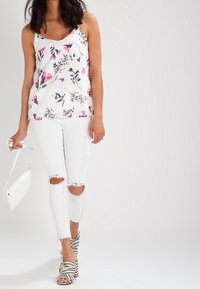 Floral print camisole in white with pink and navy accents, paired with distressed white jeans and black-and-white striped heels.
