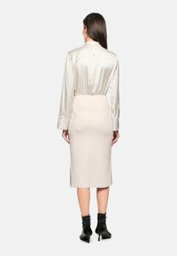 Seidenbluse in Creme mit einem passenden, figurbetonten Creme-Bleistiftrock. Das Outfit hat lange Ärmel, einen Knopfverschluss auf der Rückseite und einen hohen Schlitz am Rock.