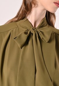 Olivgrüne Bluse mit Schleife am Hals, plissiertem Detail und weichem, glattem Stoff. 