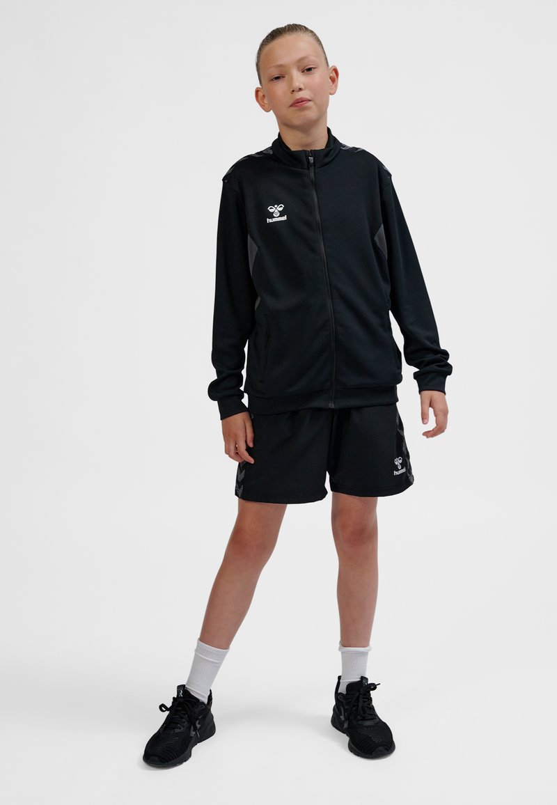 Svart sportoverall med zip-up jacka och shorts, med grå detaljer och logotyp. Texturerat, lättviktigt tyg.