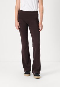 Brune breddebukser med en bred elastisk talje, lavet af blødt stof. Båret med en hvid t-shirt og sorte sneakers.