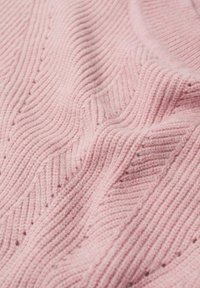 Tissu tricoté rose doux avec des motifs côtelés et en chevron créant des vagues texturées et de petites perforations partout.