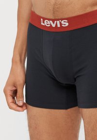 Boxers noirs avec une taille rouge arborant le logo Levi's. Le tissu semble doux avec une texture lisse et un ajustement près du corps.