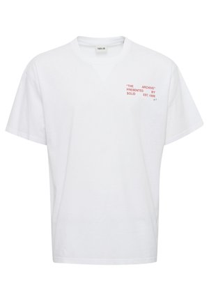 T-shirt en coton blanc avec une coupe décontractée. Présente un col en V et un texte rouge : "L'ARCHIVE" et "PRÉSENTÉ PAR SOLID EST. 1999" sur le devant.