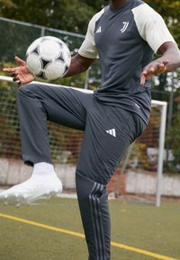 Conjunto deportivo en gris con acentos en blanco; cuenta con una camiseta de manga corta y pantalones ajustados con tres rayas. Un balón de fútbol está en juego.