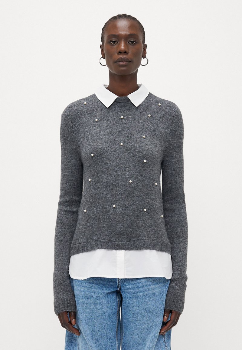 Grauer Strickpullover mit weißem Kragen, der verstreute Perlenakzente aufweist. Lange Ärmel und eine leicht lockere Passform.