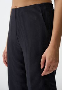 Zwarte pinstripe broek met een op maat gesneden pasvorm, zachte stof, zijzakken en een platte tailleband voor een gestroomlijnde uitstraling.