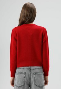 Pull rouge en maille avec col rond et manches longues, doté d'une texture douce et d'un ourlet côtelé. Assorti à un jean gris taille haute.