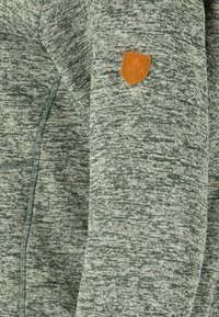 Grågrön sweatshirt med en texturerad tyg, med en sydd dragkedja och en brunt läderpatch med logotyp på ärmen.
