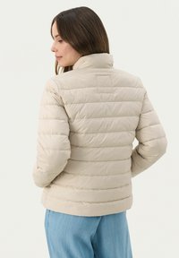 Giacca imbottita beige con cuciture orizzontali, colletto alto e forma leggermente aderente. Tessuto morbido e materiale leggero adatto per essere indossato a strati.