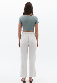 Camiseta corta de color verde claro combinada con pantalones holgados en color blanco roto que cuentan con una cinturilla elástica y bolsillos traseros. Textura suave en toda la prenda.