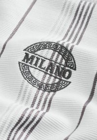 Tissu blanc texturé avec le texte noir "MILANO" brodé, encadré par une bordure décorative circulaire avec des rayures grises verticales.