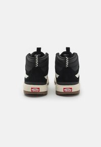 Zapatillas altas negras que combinan materiales de ante y tela, con acentos crema, suela texturizada y un distintivo tirador a cuadros.